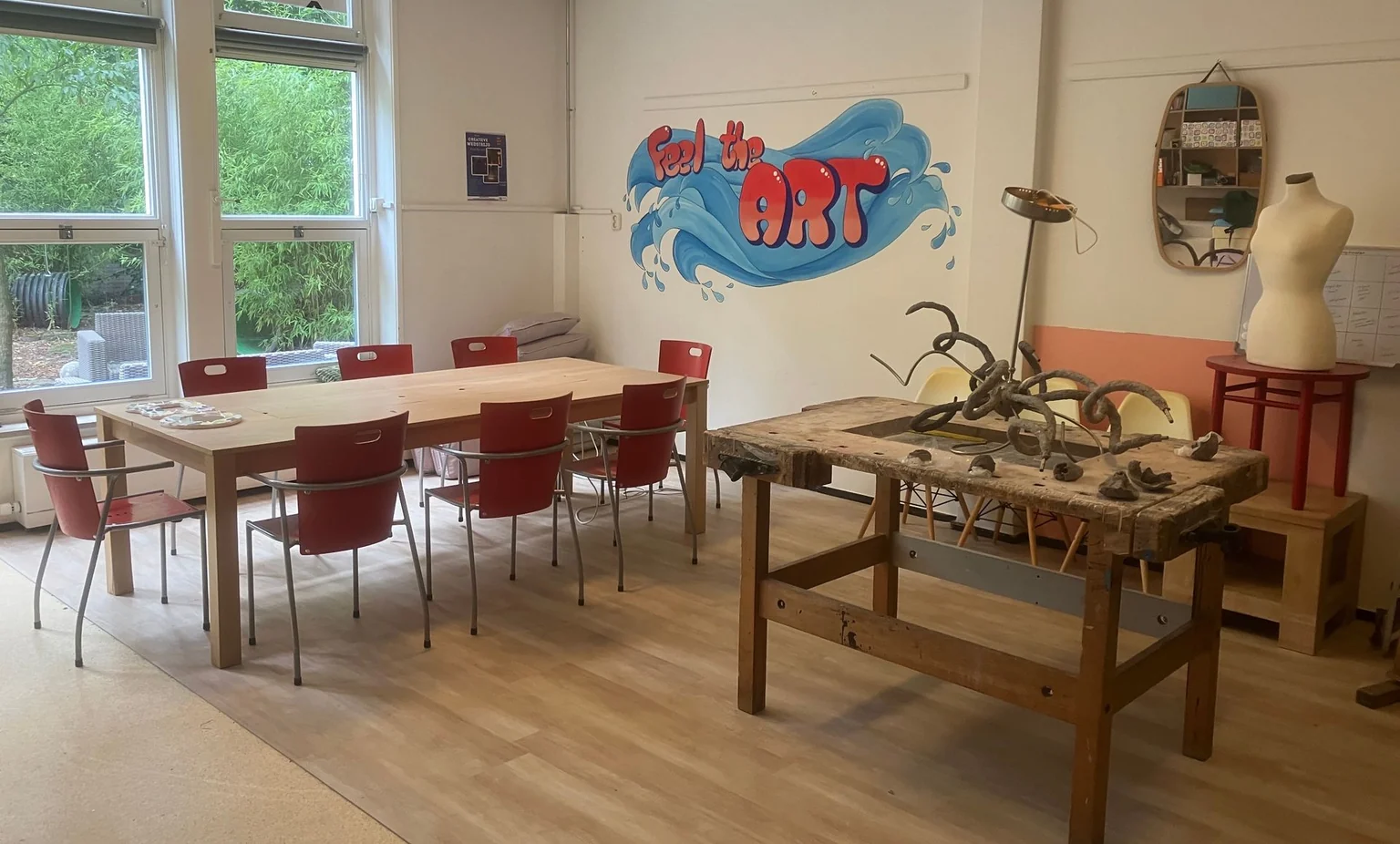 De werkplaats van Studio Kokosnoot met werktafels, gereedschap en een kleurrijke muurschildering.