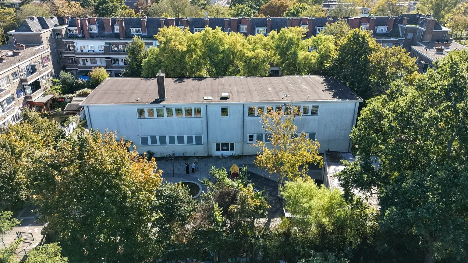 Het gebouw van De Kokosnoot met het plein en de bomen, gezien vanuit de lucht.